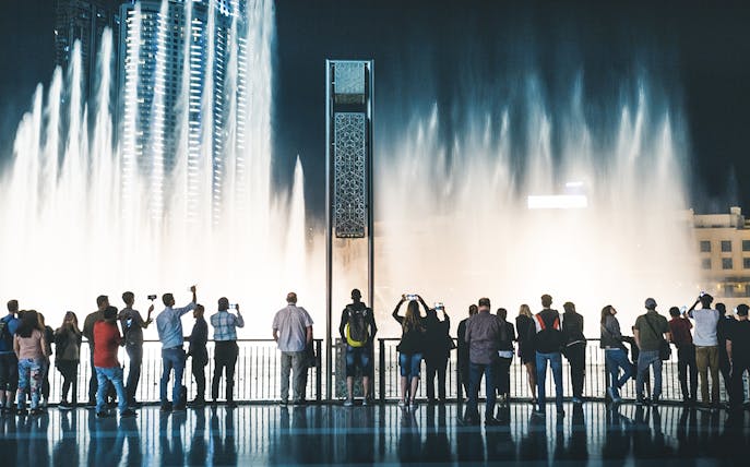 Visitors watching Dubai Fountain show from boardwalk at night.
