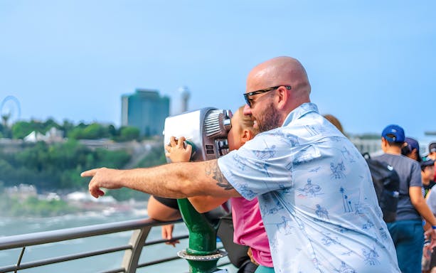 Man and child using binoculars at observation point overlooking cityscape.