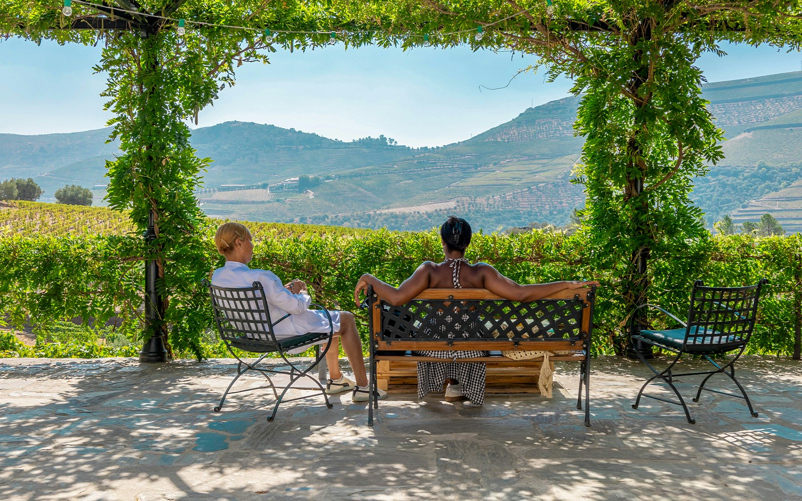 Tourists relaxing on a bench with a view of Douro Valley vineyards.