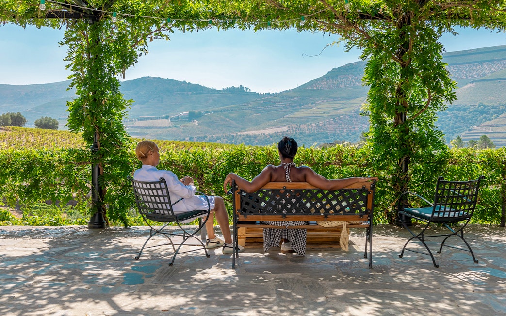 Tourists relaxing on a bench with a view of Douro Valley vineyards.