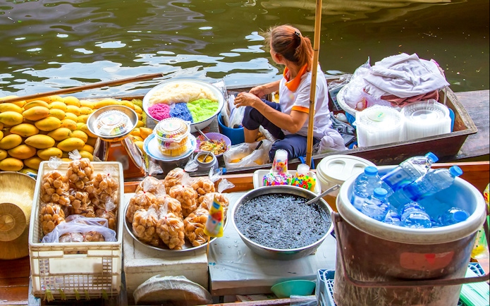 Vendor selling colorful desserts and snacks at Damnoen Saduak Floating Market, Thailand.