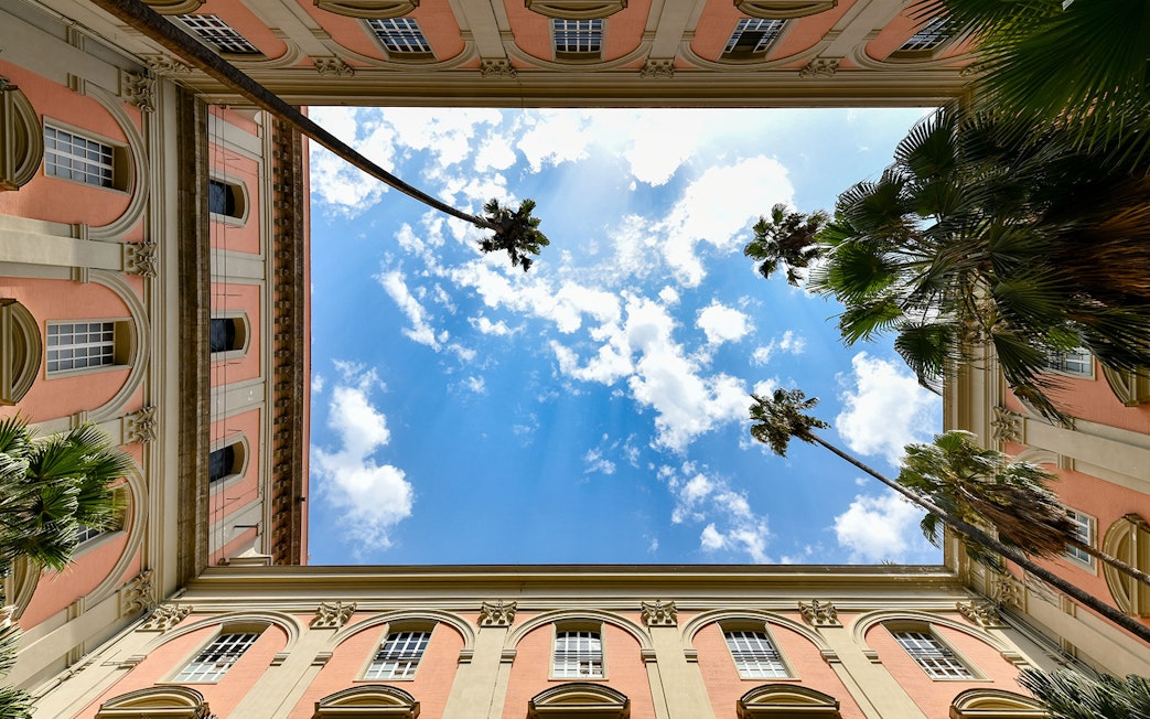 Courtyard view of Naples National Archaeological Museum with palm trees and blue sky.
