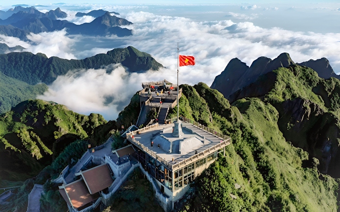 Sun World Fansipan Legend summit with flag, surrounded by lush mountains and clouds in Vietnam.