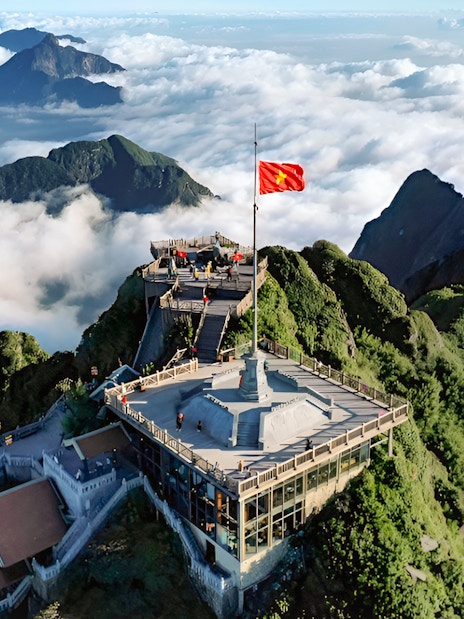 Sun World Fansipan Legend summit with flag, surrounded by lush mountains and clouds in Vietnam.