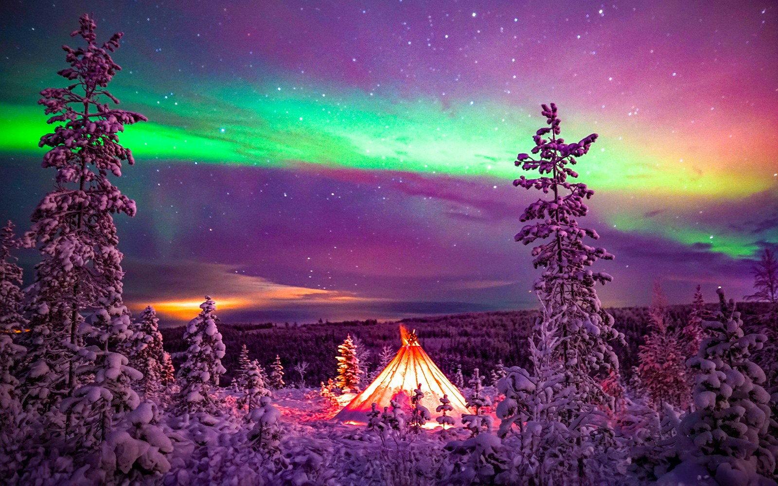 Northern Lights over snowy Rovaniemi landscape with illuminated tent during guided tour.