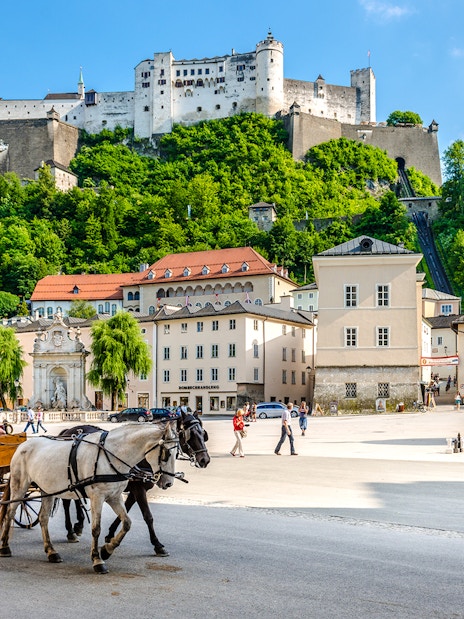 Horse-drawn carriage in Salzburg's old town with Hohensalzburg Fortress, Austria.