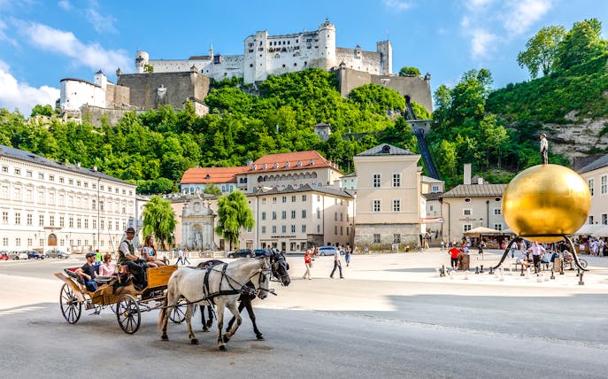 Horse-drawn carriage in Salzburg's old town with Hohensalzburg Fortress, Austria.