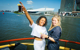 Guests enjoying drinks on a Dutch Pancake cruise in Amsterdam with cityscape views.