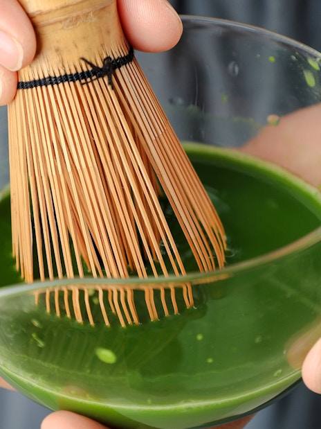 Whisking matcha with a chasen in a clear bowl.
