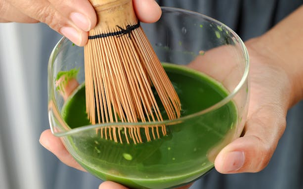 Whisking matcha with a chasen in a clear bowl.