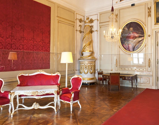 Imperial Apartments Sisi Museum interior with ornate red furniture and chandelier.