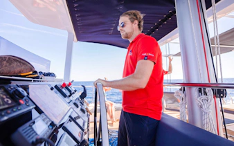 Catamaran crew member steering during sunset cruise with ocean view.