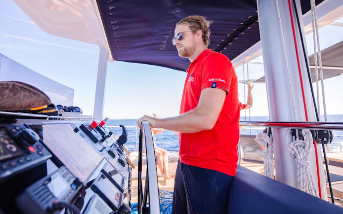 Catamaran crew member steering during sunset cruise with ocean view.