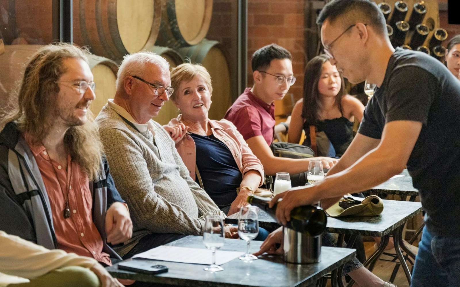 Guests enjoying wine tasting at Yarra Valley winery with barrels in the background.