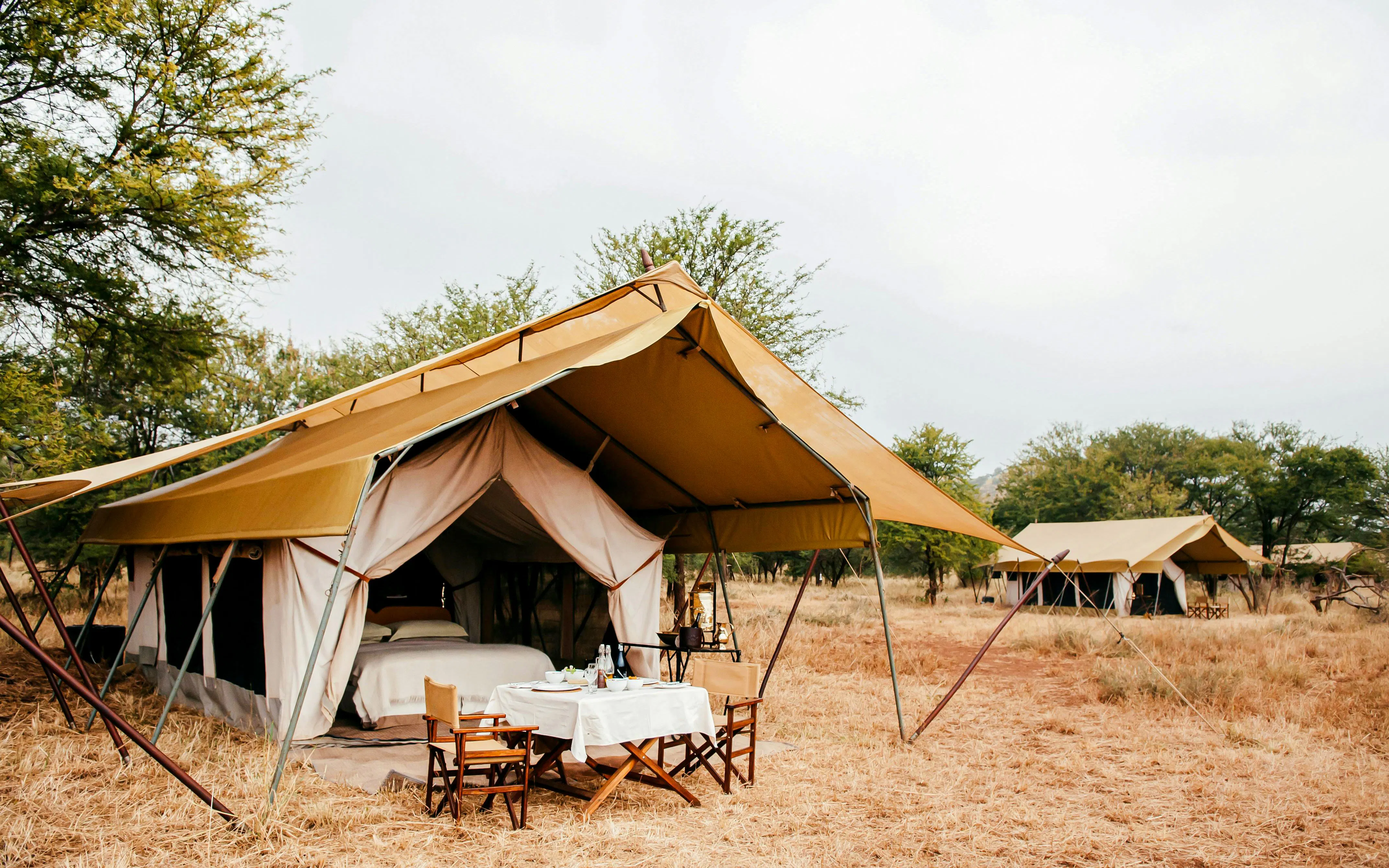 Luxury safari tent camp with dining setup in African savanna.