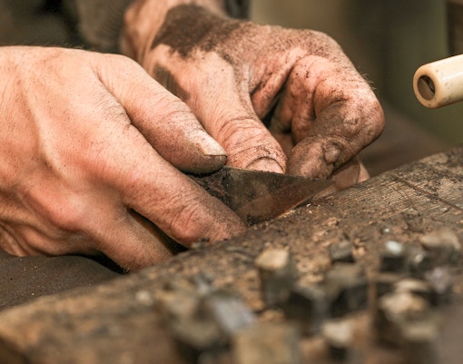 A craftsman making rosary beads using certain sharp tools and a flat platform.
