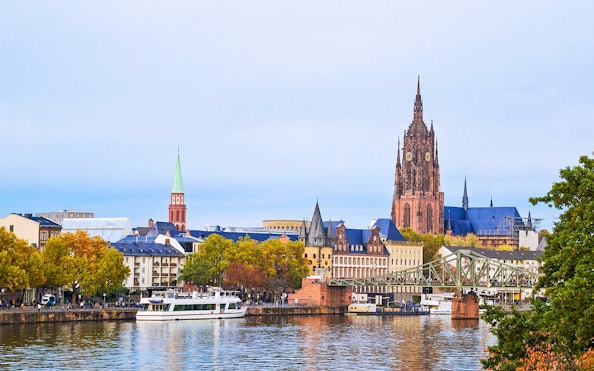 Cityscape of Frankfurt with a cruise boat on the Main River, featuring the Frankfurt Cathedral.