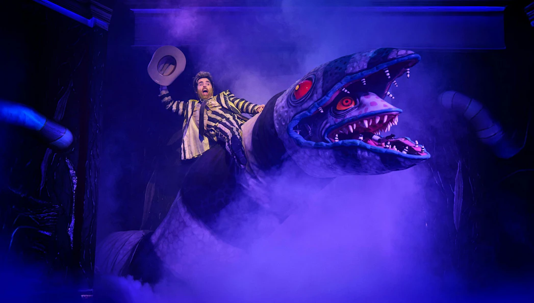 Beetlejuice performer on giant snake prop during Westend show.