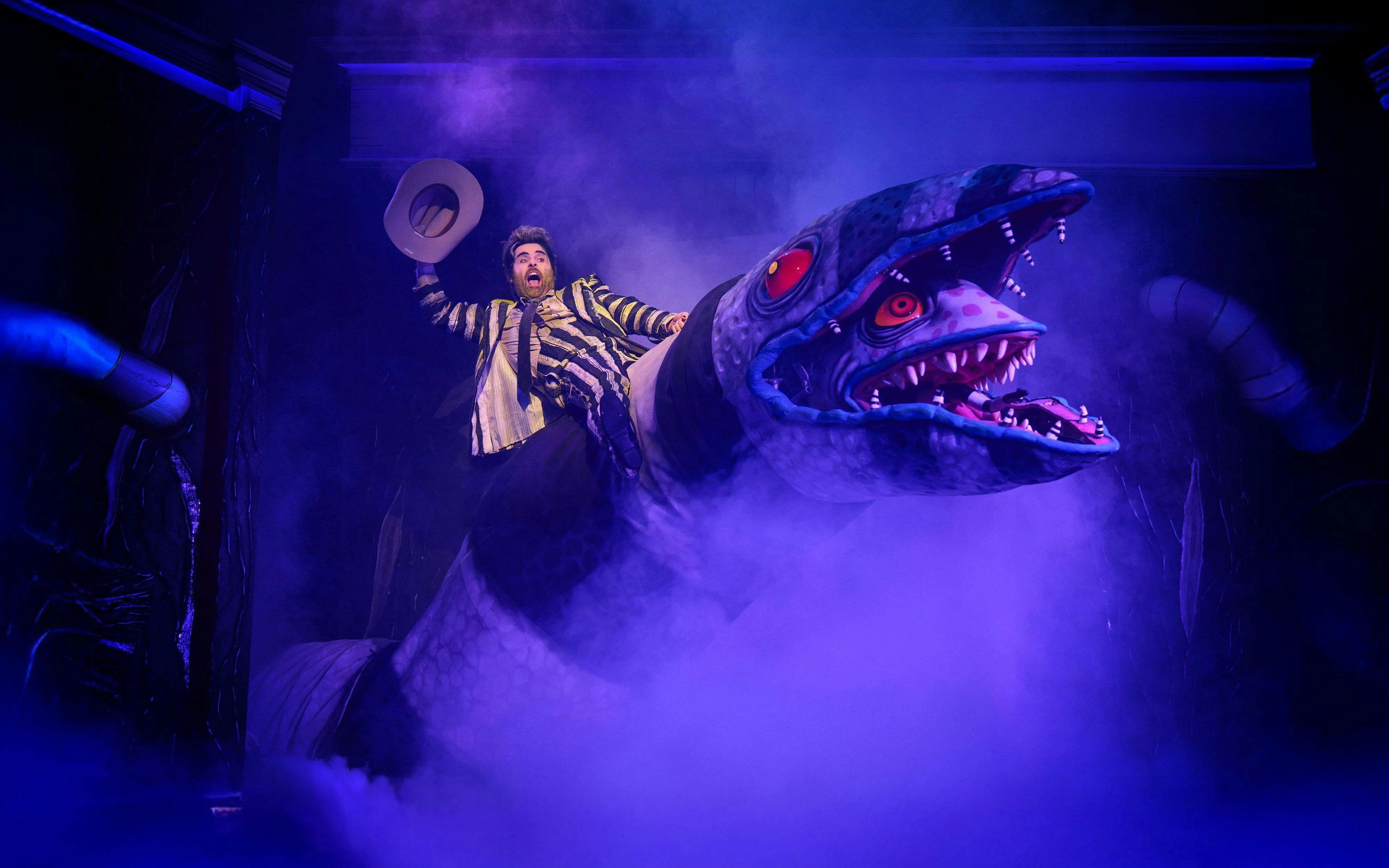 Beetlejuice performer on giant snake prop during Westend show.