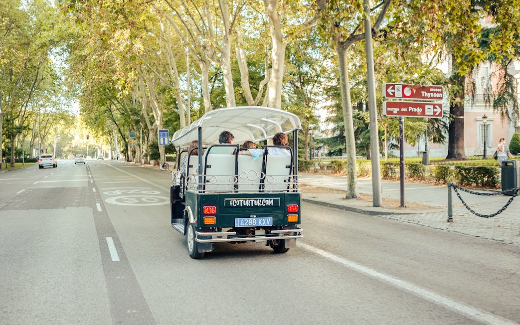Eco-friendly electric tuk-tuk on a tree-lined street in Madrid, Spain.