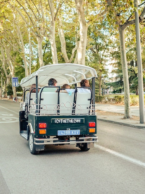 Eco-friendly electric tuk-tuk on a tree-lined street in Madrid, Spain.