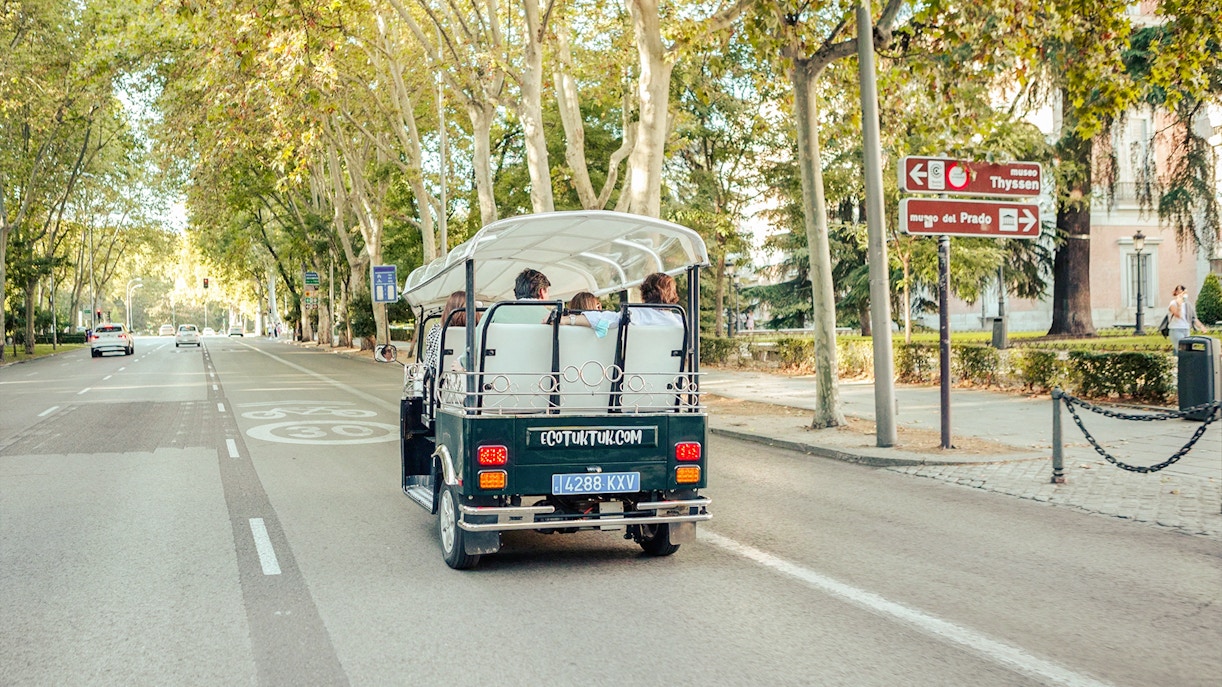 Eco-friendly electric tuk-tuk on a tree-lined street in Madrid, Spain.