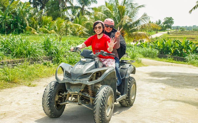 ATV riders on a dirt path in Ubud, surrounded by lush greenery.