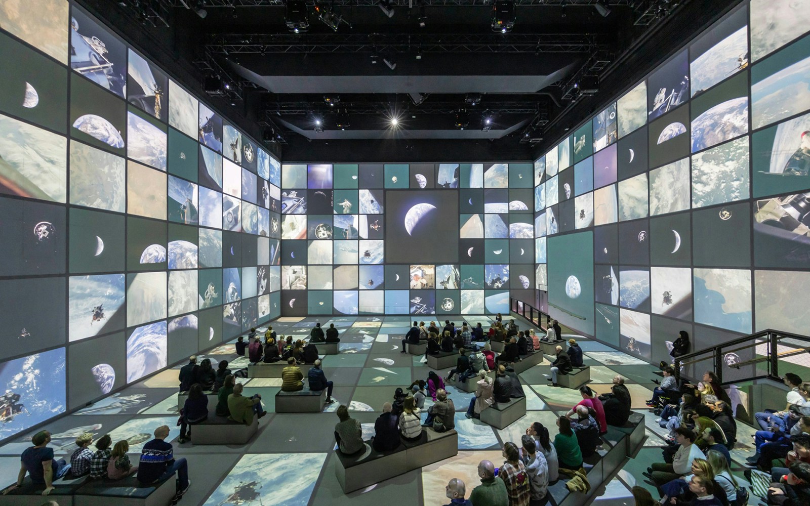 Visitors seated in a digital exhibition room with space-themed projections, part of The Moonwalkers tour.