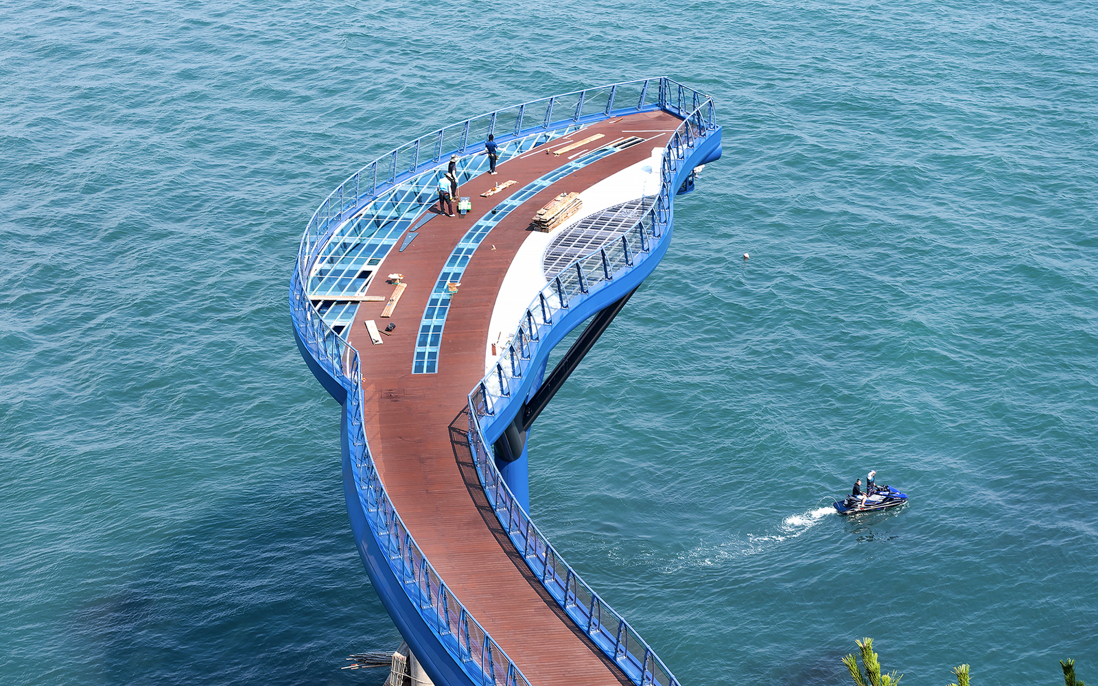 Blueline Park Sky Capsule platform over ocean in Busan, South Korea, with people and jet ski nearby.