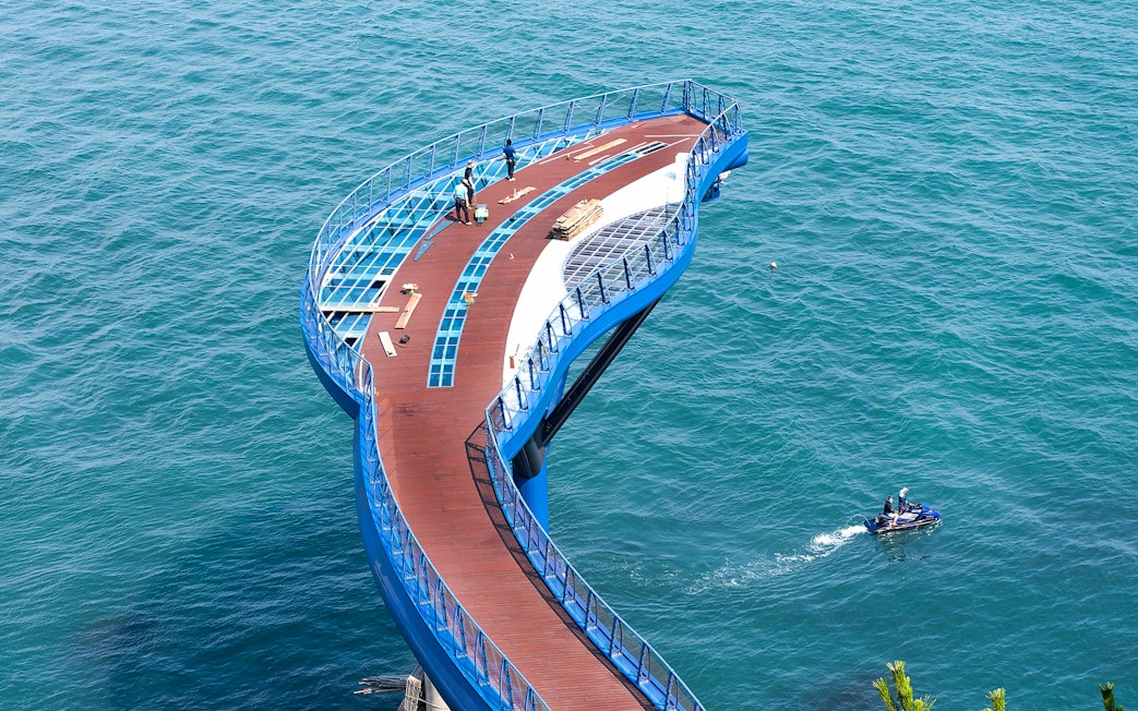 Blueline Park Sky Capsule platform over ocean in Busan, South Korea, with people and jet ski nearby.