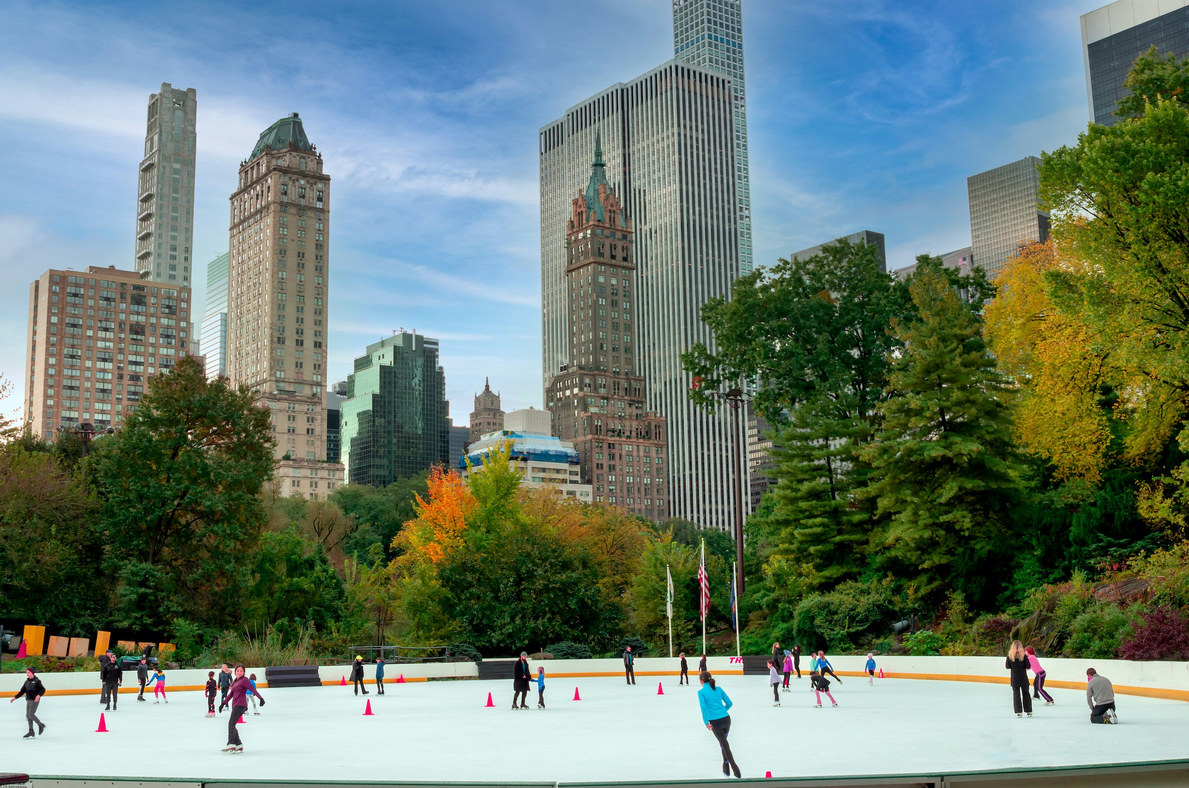 Skaters at Wollman Ice Rink in Central Park, New York, with city skyline in the background.