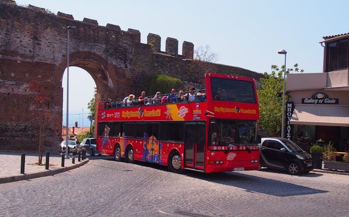 Thessaloniki hop-on hop-off bus near ancient city wall arch.