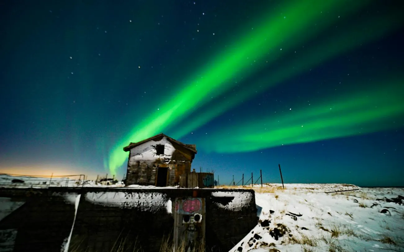 Northern Lights over snowy landscape with old building, Reykjavik Jeep tour.