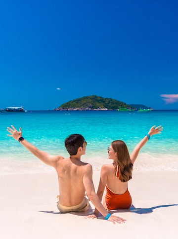 Couple sitting on Similan Islands beach with clear blue water and island view.
