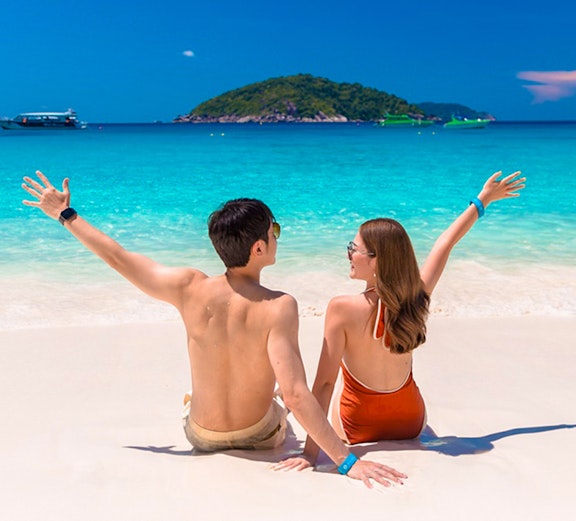 Couple sitting on Similan Islands beach with clear blue water and island view.