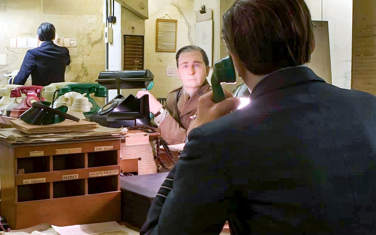 Man in military uniform at desk with vintage telephones, Churchill War Rooms tour.