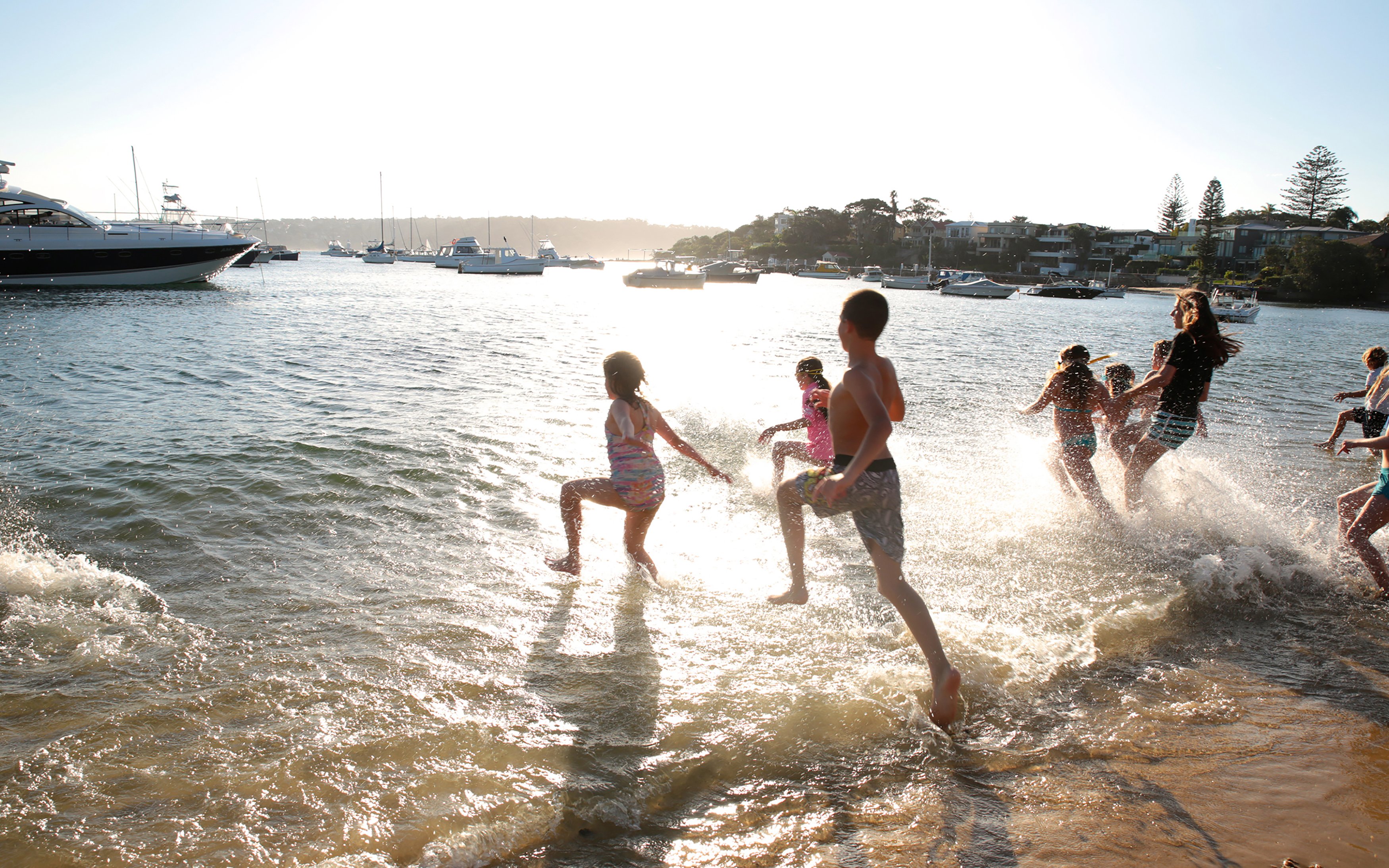 Children playing in the water at sunset near boats in Sydney harbor.
