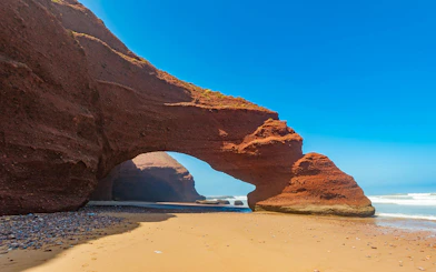 Red rock arch formations on Legzira Beach, Morocco, with ocean waves in the background.