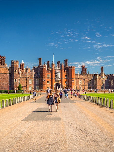 Tourists walking towards Hampton Court Palace in London on a sunny day.