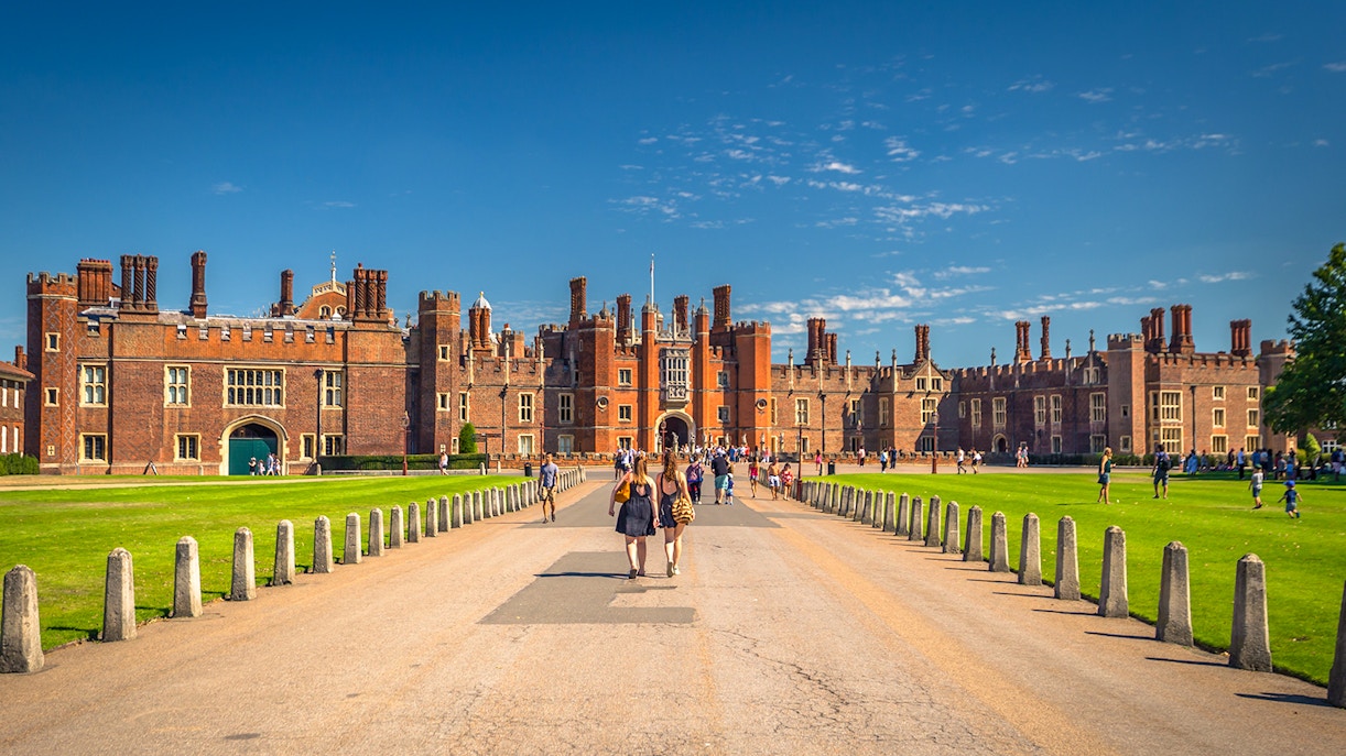 Tourists walking towards Hampton Court Palace in London on a sunny day.