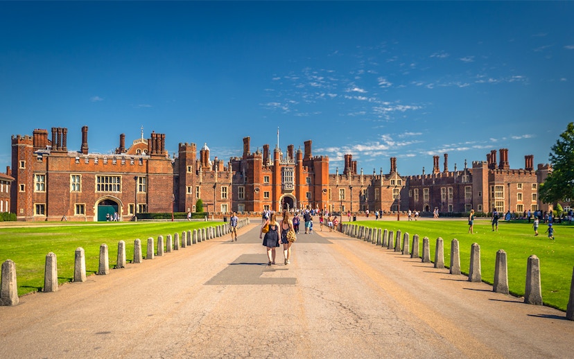 Tourists walking towards Hampton Court Palace in London on a sunny day.