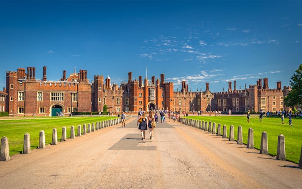 Tourists walking towards Hampton Court Palace in London on a sunny day.