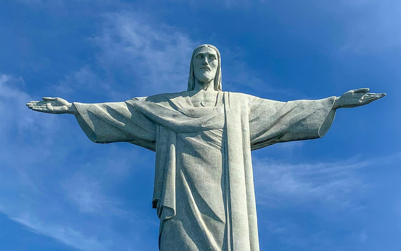 Christ the Redeemer statue with arms outstretched against blue sky, Rio de Janeiro.