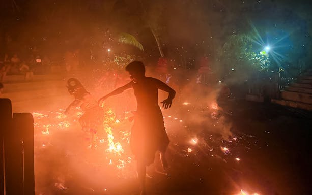 Performer amidst smoke and flames during fire dance at Tanah Lot Temple, Bali.
