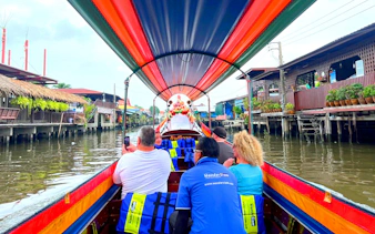 Longtail boat ride through Bangkok canal with passengers viewing traditional stilt houses.