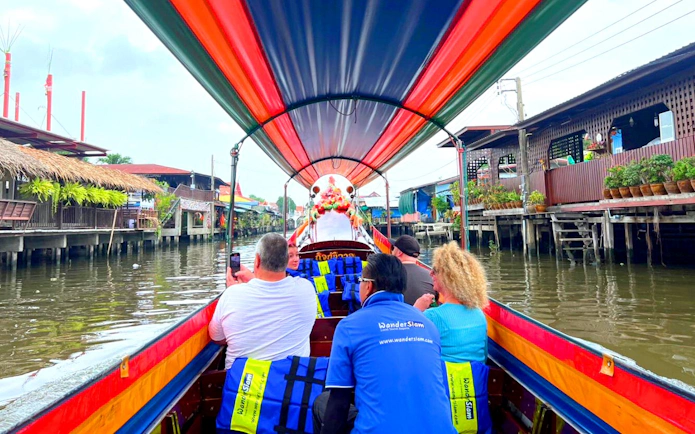 Longtail boat ride through Bangkok canal with passengers viewing traditional stilt houses.