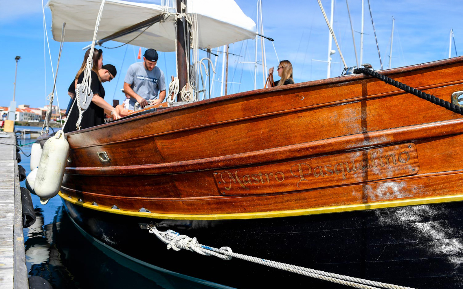 Wooden sailboat docked for Asinara Island excursion with people preparing on deck.