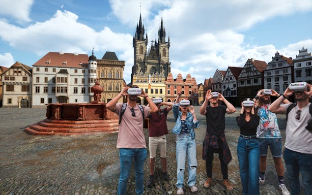 Tourists using VR headsets in Prague's Old Town Square with Týn Church in background.