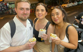 Tourists enjoying banh mi on Saigon street food scooter tour.