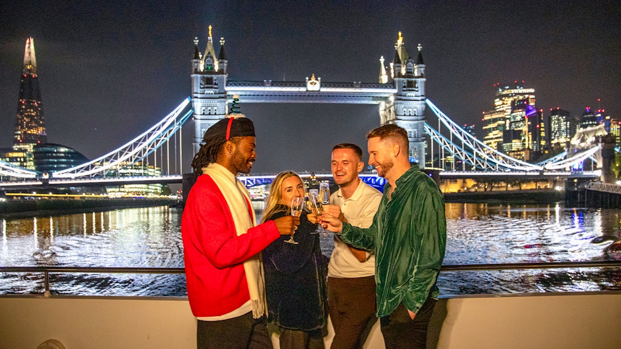 Guests enjoying a Christmas dinner party on a Thames River cruise with Tower Bridge in the background.